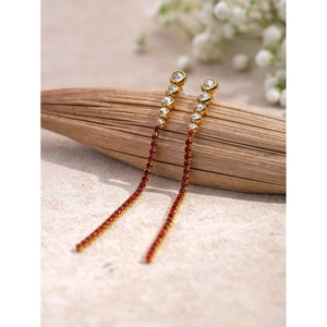 Macro shot of gold-plated tassel earrings with white zircon and red crystal details