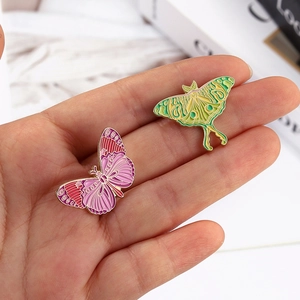 Detail of colorful butterfly and moth enamel pins held in hand to show real size