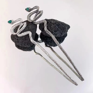 Retro silver snake hair pins with green gemstone eyes on dark volcanic stone