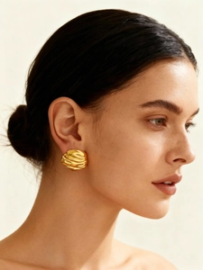Close-up of gold geometric pleated earrings with sculpted texture on model's ear