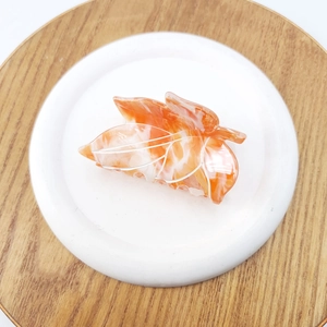 Close-up of leaf-shaped hair claw with orange and white marble pattern in a ceramic tray