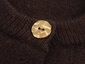 Macro shot of a textured gold button on a thick dark brown knit cardigan detail