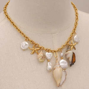 Detail van gouden ketting met zeester- schelp- en barokke parelhangers