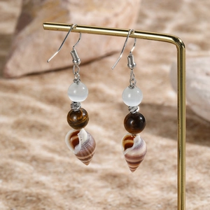 Detail view of shell earrings with tiger eye and cat eye stones on a gold stand