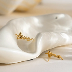 Macro shot of gold LOVE stud earrings on a wavy display stand with soft lighting