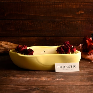 Primer plano de un portavelas amarillo ondulado con rosas rojas secas y cera