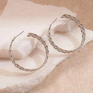 Detailed view of silver braided C-shape hoop earrings on a white quartz stone