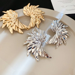 Macro shot of gold and silver pleated metal earrings in a minimalist ceramic dish