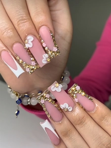 Close-up of long square press-on nails with pink base, French tips and floral gold rhinestones