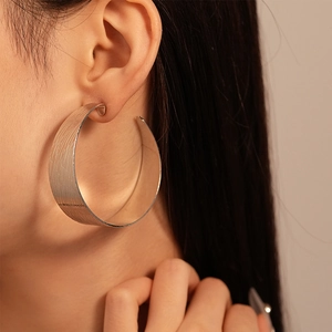 Détail macro de boucles d'oreilles créoles en métal brossé argenté portées par un mannequin