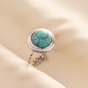 Detail view of adjustable silver metal ring with a large turquoise stone on beige fabric