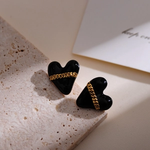 Detailed close-up of heart-shaped black earrings with gold chain link on stone background