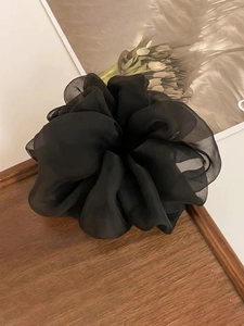 Detailed view of an oversized black mesh organza scrunchie with soft pleats on wood