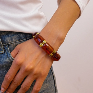 Close-up of amber resin bead bracelet with gold spacers worn on wrist in a casual pose