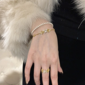 Detail of layered gold floral bracelet and pearl jewelry set worn on white fur background
