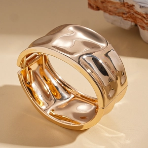 Detail view of gold metal cuff bracelet with irregular hammered texture and hinge closure
