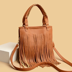Caramel brown tassel handbag with woven handle and fringe details shown on a pedestal