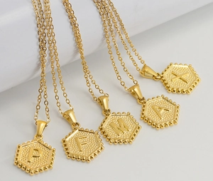 Close-up of golden stainless steel hexagonal pendants with embossed letters P F M A and X