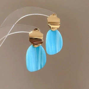 Detailed close-up of blue resin and gold metal geometric earrings on a display