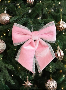 Pink velvet Christmas bow with silver glitter edges on a decorated holiday tree