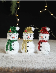 Close-up of glittery snowman ornaments in green, gold, and red with hanging strings