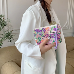 Close-up of floral canvas cosmetic bag with purple braided wristlet held by a model
