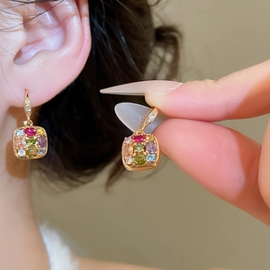 Close-up of gold square earrings featuring colorful gemstones worn by model