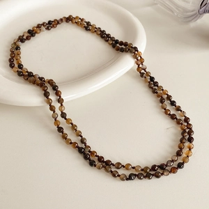Detail of bohemian layered necklace with brown agate beads on white ceramic plate