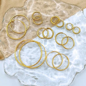 Various sizes of gold-plated stainless steel hoop earrings on luxury satin background