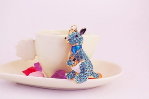 Detail of a kangaroo keychain with blue rhinestones and gold finish on a soft pink background