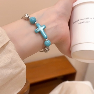Macro detail of sky blue turquoise cross bracelet with silver floral beads on wrist