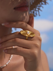 Detail of a gold striped ring with a pearl inlay on a model against a blue sky background
