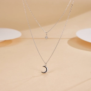 Detail of silver double-layered necklace with sparkling star and polished moon pendants