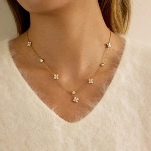 Nahaufnahme der goldenen Kleeblatt-Kette mit Zirkon-Anhängern auf beige Pullover