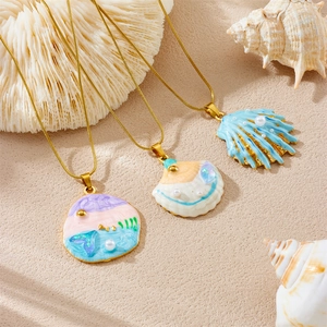 Ocean style gold necklaces with enamel shell pendants and pearls on sand beach