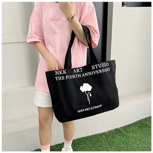Lifestyle shot of large black canvas tote bag with white floral art and studio lettering