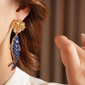 Detail of vintage gold flower earring with blue enamel fish pendant worn by model