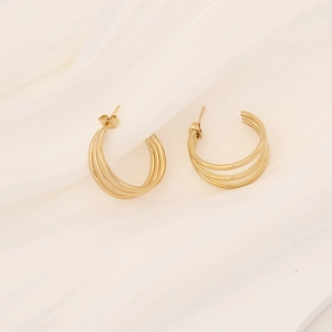 Detailed close-up of golden triple-hoop geometric C-shaped earrings on white fabric