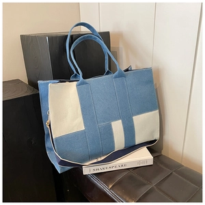 Detail of blue denim and beige canvas tote bag with white stitching and wide strap