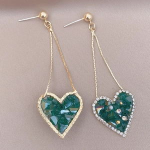 Vintage gold heart earrings with deep green crystals on a beige textured background