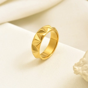 Polished gold faceted ring with pyramid texture on white marble and soft fabric