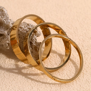 Polished 18K gold-plated stainless steel bangles in three widths on white stone