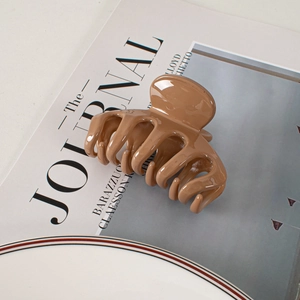 Glossy brown minimalist shark hair claw clip placed on a magazine in a lifestyle setting