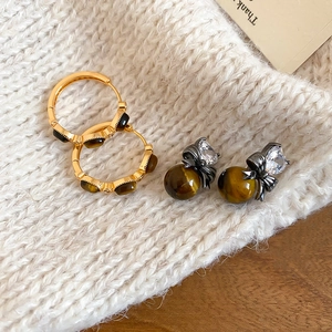 Macro shot of tiger eye stone earrings and black bow studs on white knit sweater fabric