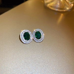 Macro shot of emerald green oval stud earrings with sparkling zircon halo on silver base