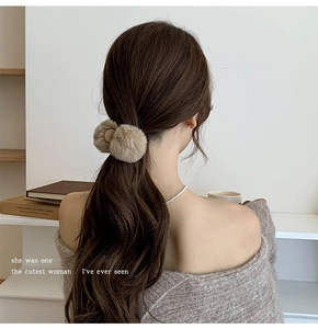 Close-up of a plush beige pom-pom hair claw clip worn on a messy bun hairstyle