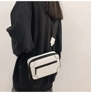 Close-up of white mini suitcase crossbody bag with black corner protectors and wide strap