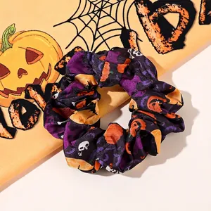 Close-up of purple Halloween scrunchie with pumpkin and skull prints in satin fabric