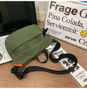 Detail of army green nylon crossbody bag with black adjustable strap and orange brand label