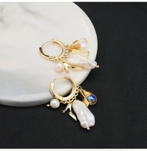 Detail of handmade gold earrings featuring irregular pearls and shoe charms on marble